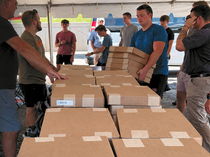 Volunteers under a tent stacking boxes of refurbished computers at a distribution day.