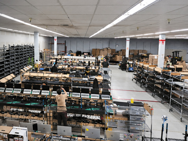 Regadget’s refurbishing floor from above: long benches of laptops being tested, shelving along the wall and technicians at work.