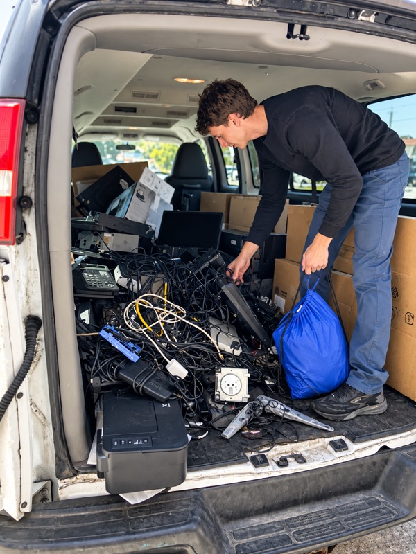 A Regadget team member loading a van with retired printers, monitors, desk phones and cables at a pickup.